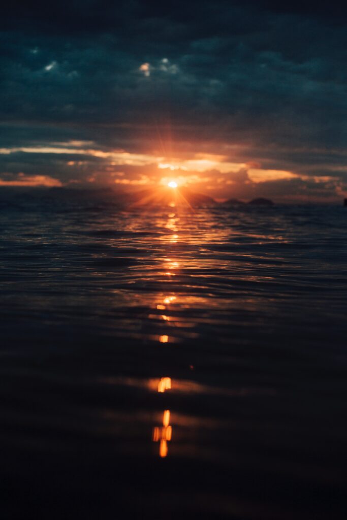 Breathtaking sunset over rippling sea with warm orange gold tones and dramatic moody sky wallpaper