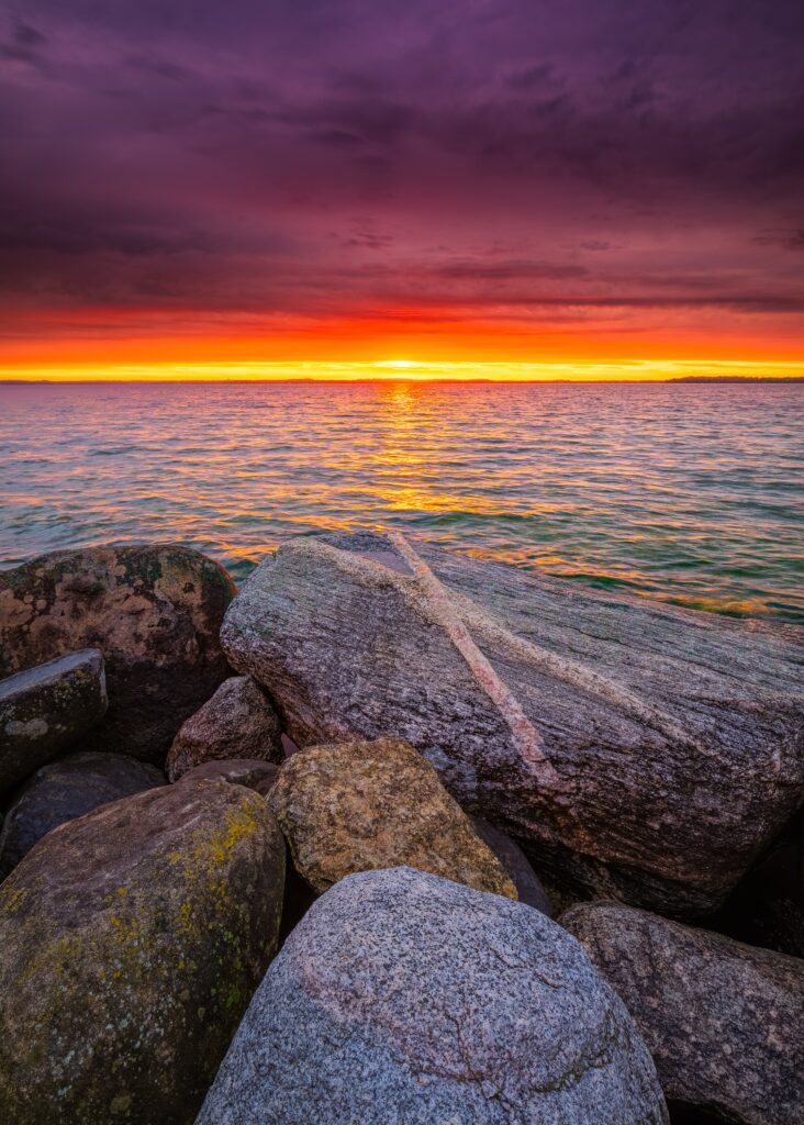 Textured stones on rocky shore under vivid sunset sky with calm sea horizon wallpaper background