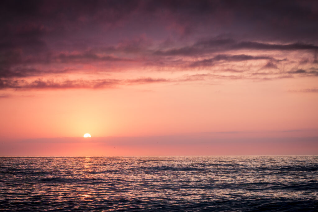 Tranquil sea at sunset with pastel sky and gentle ripples reflecting pink orange and purple hues Wallpaper