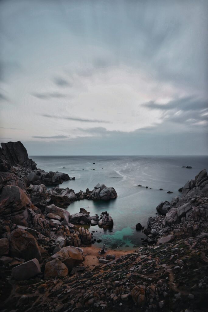 Serene sunset over calm sea with rugged rocks and soft blue orange sky coastal wallpaper background