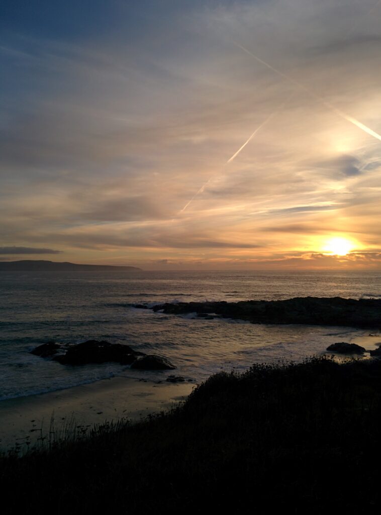 Sunset over calm shore with golden reflections soft clouds and dark rock silhouettes wallpaper background