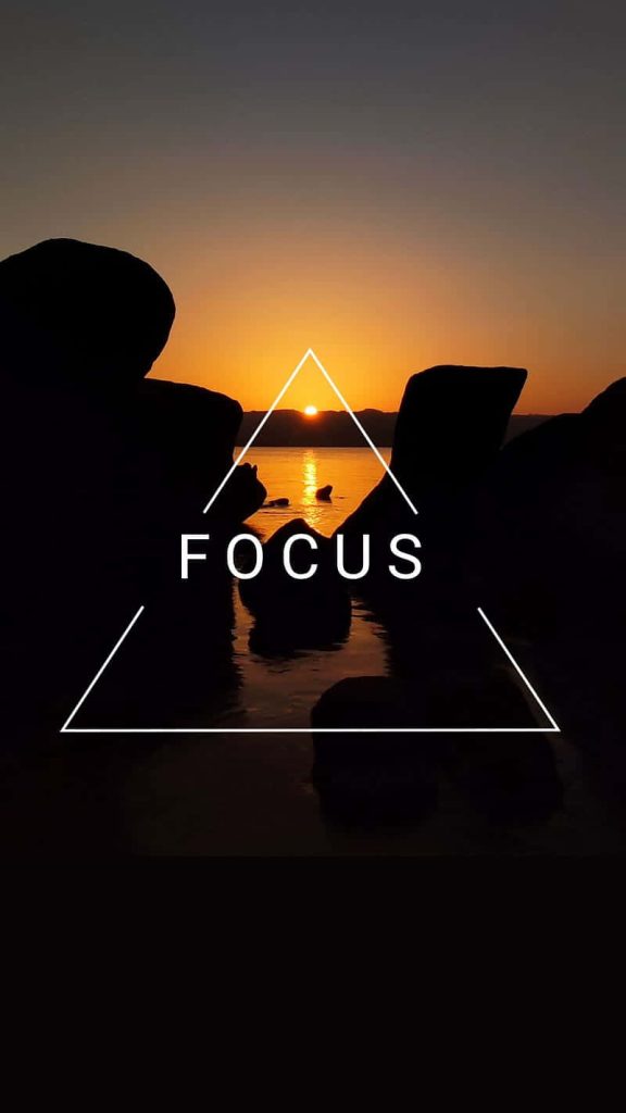 Serene sunset over water with dark rocks and white triangle overlay featuring word focus Wallpaper