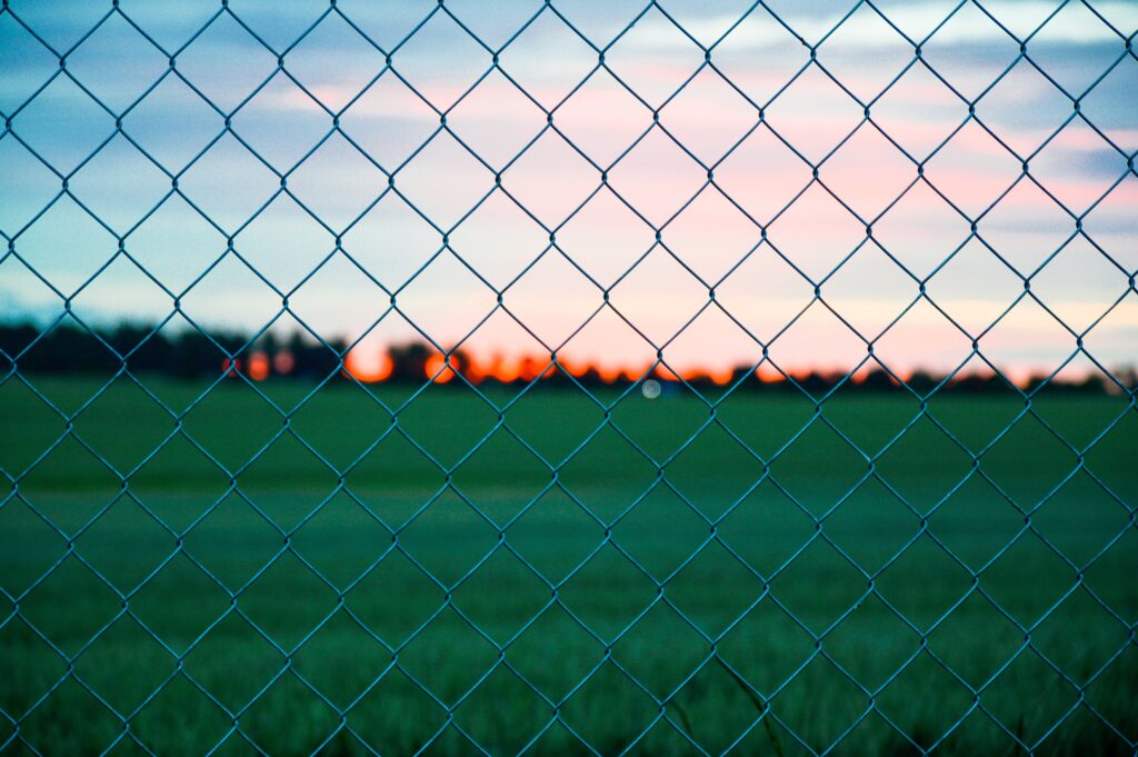 Close-up wire mesh fence with geometric pattern against grassy field and vibrant sunset sky wallpaper