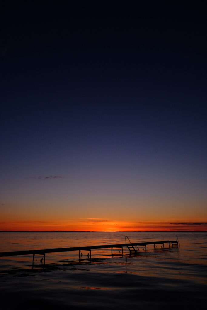 Serene pier at sunset over calm sea with warm orange gold hues blending into twilight blues wallpaper