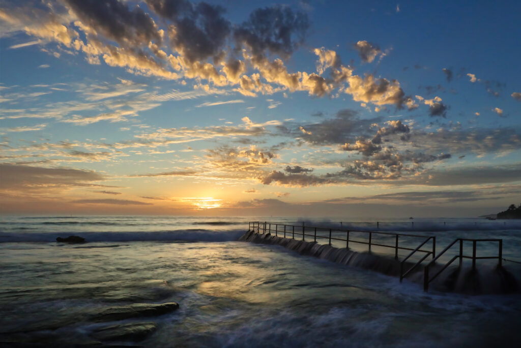 Serene pier over restless sea at sunset with gentle waves and dramatic cloudscape wallpaper background