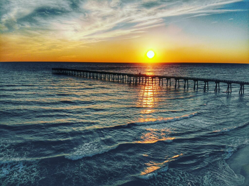 Serene pier at sunset over calm sea with warm orange gold hues and gentle waves wallpaper background
