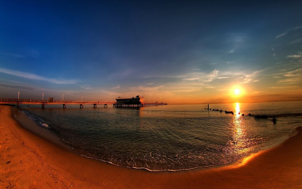 Panoramic sunset pier over calm waters golden hues reflecting on tranquil sandy coastline wallpaper