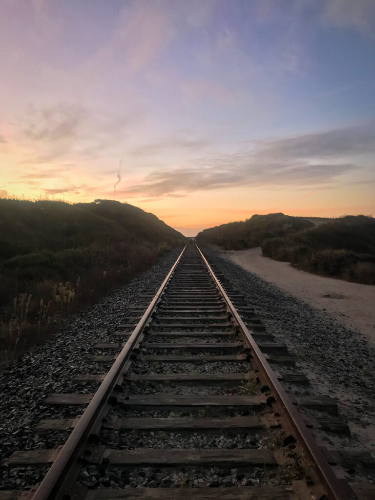 Serene railroad track at twilight surrounded by lush trees and warm sunset hues wallpaper