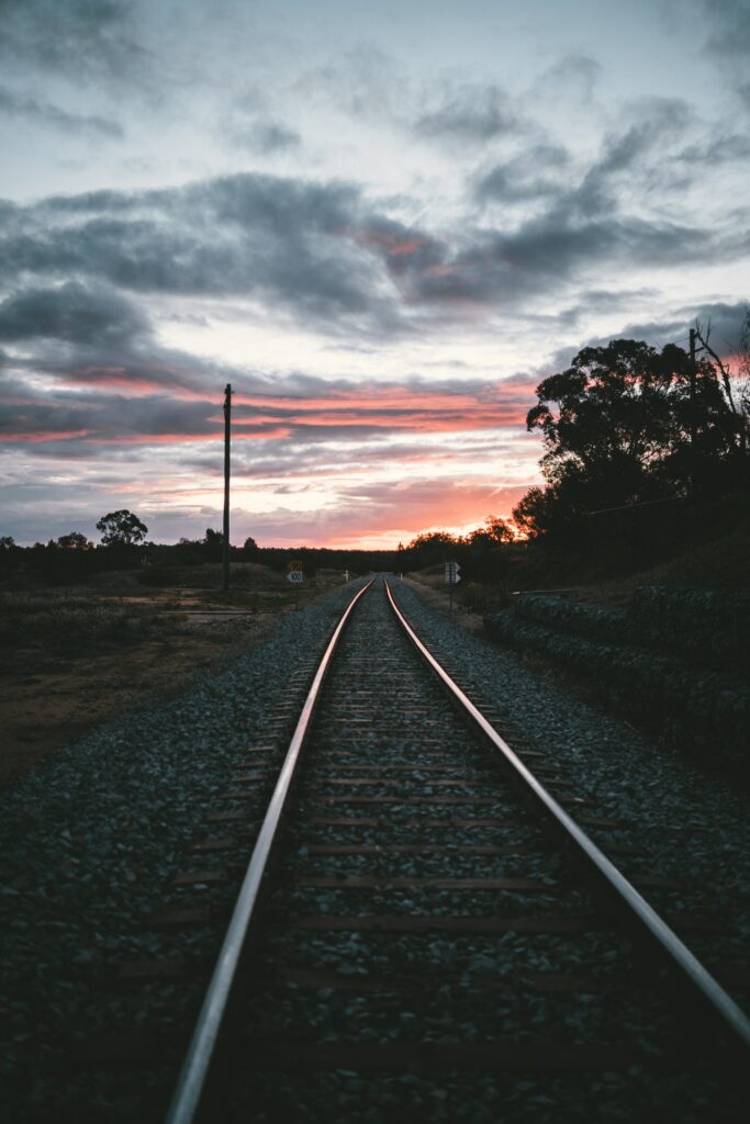 Sunset railroad with curved steel rails pebbles dramatic clouds pink orange sky silhouettes trees Wallpaper