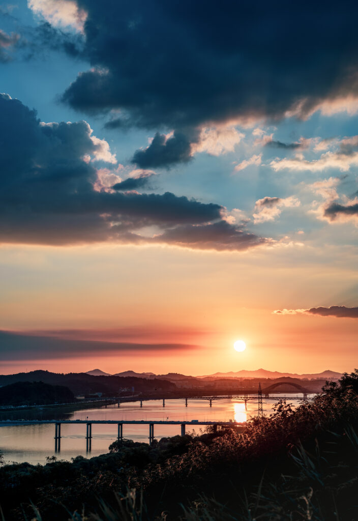 Serene river flowing under long bridge at sunset with orange pink sky and distant hills wallpaper