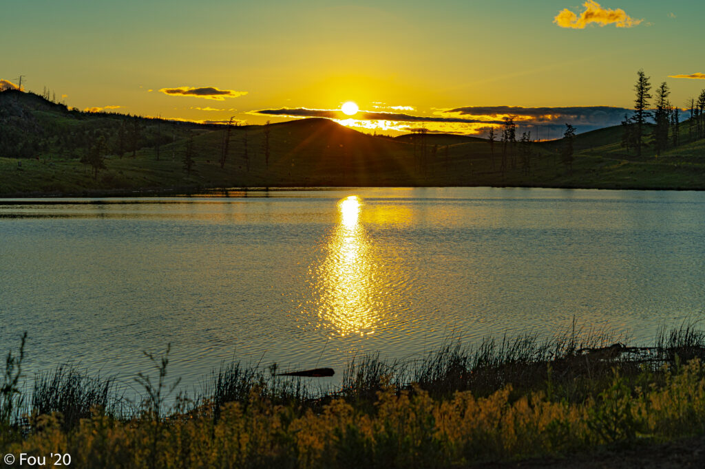 Serene sunset over calm river with golden rays gentle hills and silhouetted trees wallpaper background
