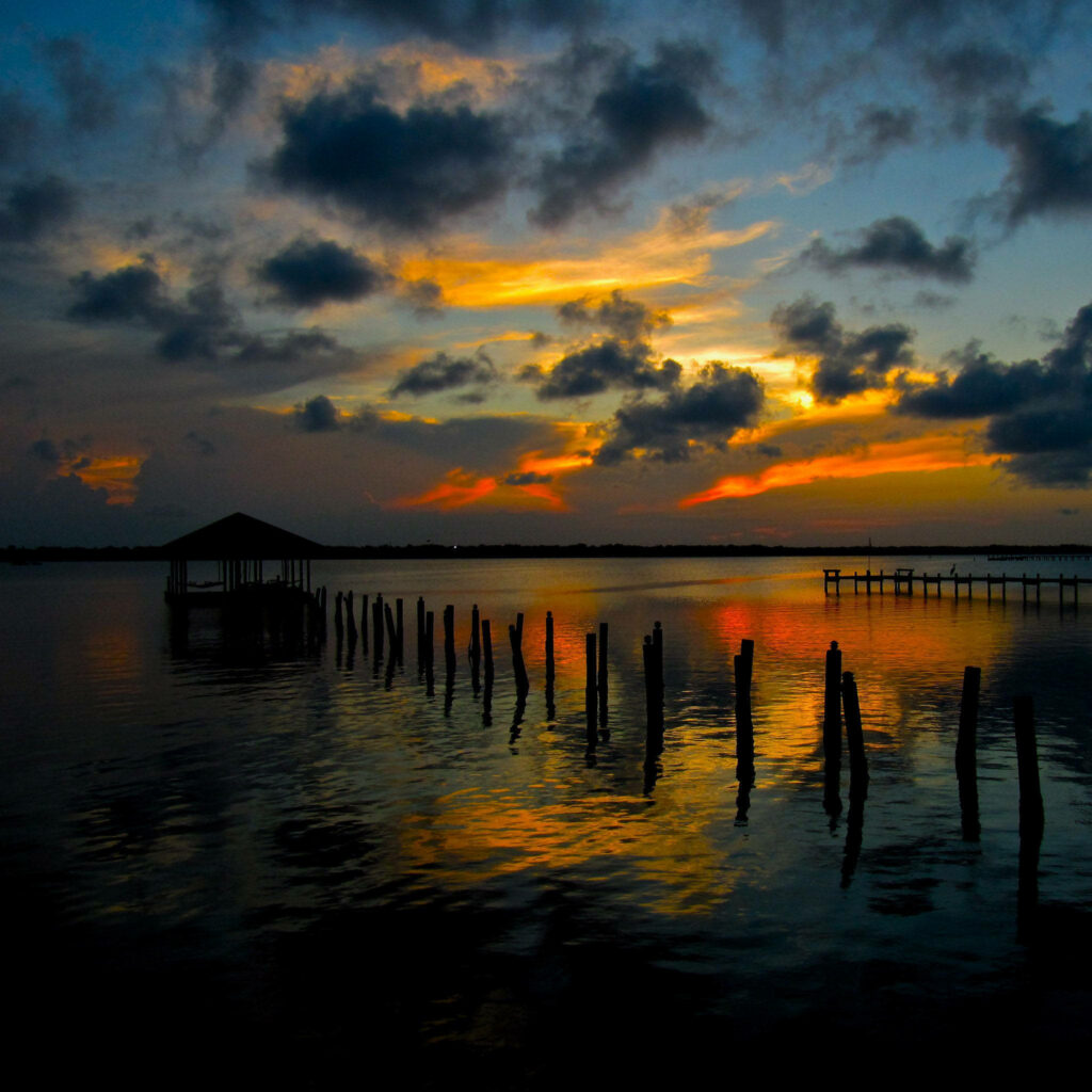 Tranquil Sunset Riverside Scene: Vivid Sky & Calm Waters Wallpaper