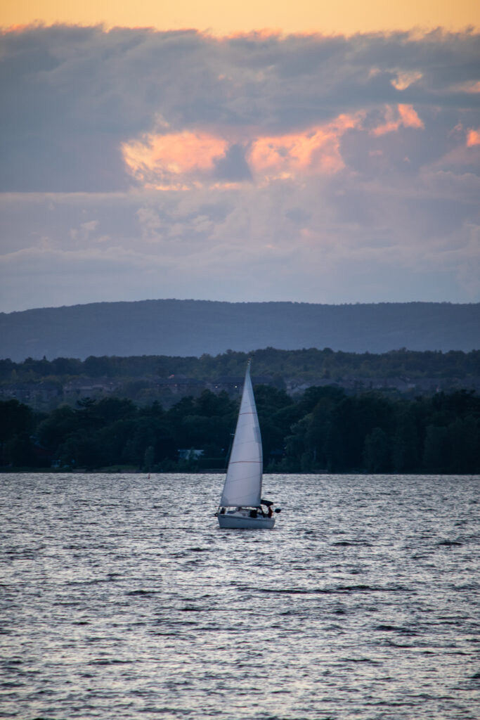 Serene sailboat on rippling sea at sunset with shadowy trees and rolling hills wallpaper background