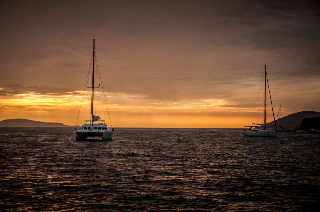 Two sailboats on calm sea at sunset with golden amber light and soft water reflections wallpaper