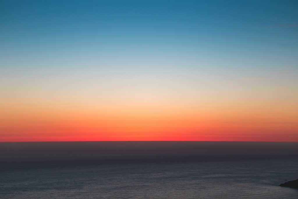 Serene sea horizon at sunset with orange red and blue hues minimalist natural wallpaper background