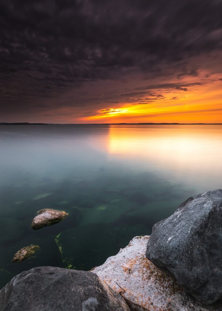Sunset sea view wallpaper with golden sky dark clouds calm water smooth rocks shoreline