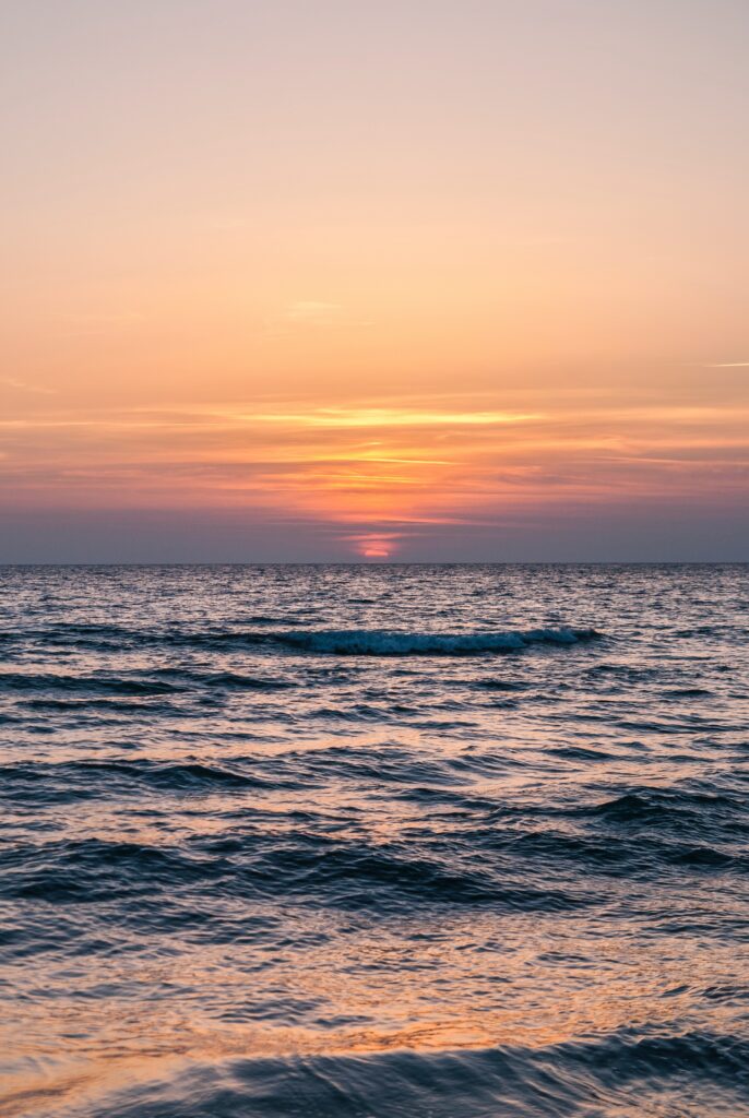 Serene sea sunset wallpaper with gentle waves reflecting orange pink purple minimalist gradient