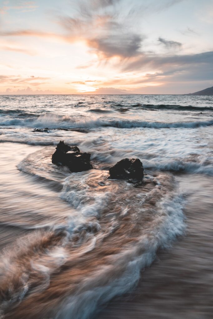 Serene sunset seascape with gentle waves, rugged rocks, and warm glowing coastal sky wallpaper
