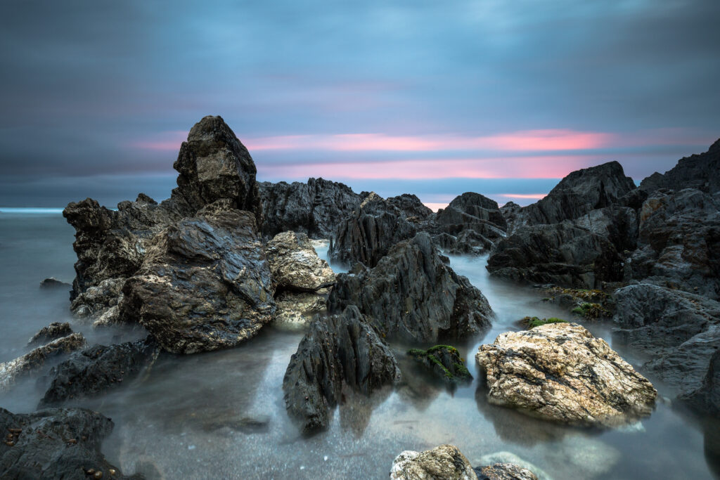 Sunset shore with rugged stones and soft water flow in pink and purple serene sky background Wallpaper