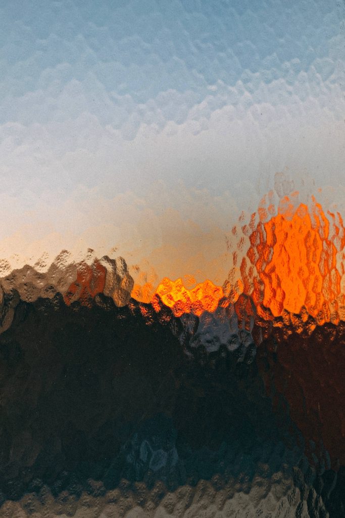 Vibrant sunset glowing through textured frosted glass with warm orange light and dark silhouettes Wallpaper