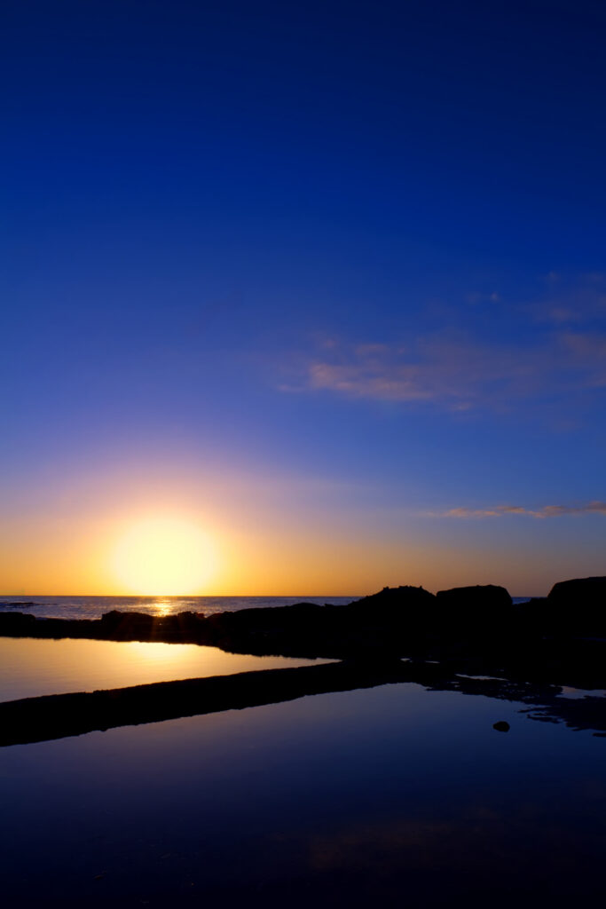 Serene sunset wallpaper with vivid blue and gold hues reflecting over calm sea and rocks