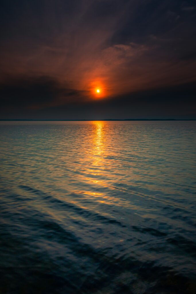 Serene sunset over ocean with warm orange reflections gentle waves and dramatic clouds wallpaper