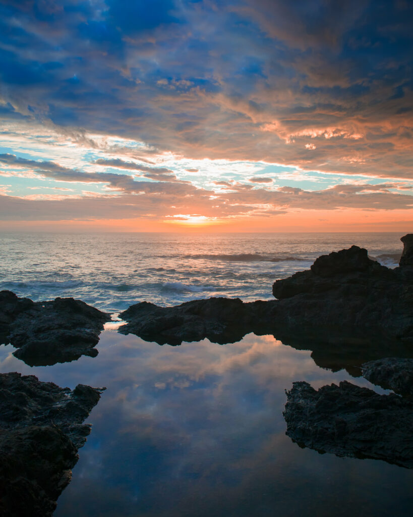 Sunset wallpaper with dramatic clouds rugged rocks tranquil sea waves vivid orange and blue hues