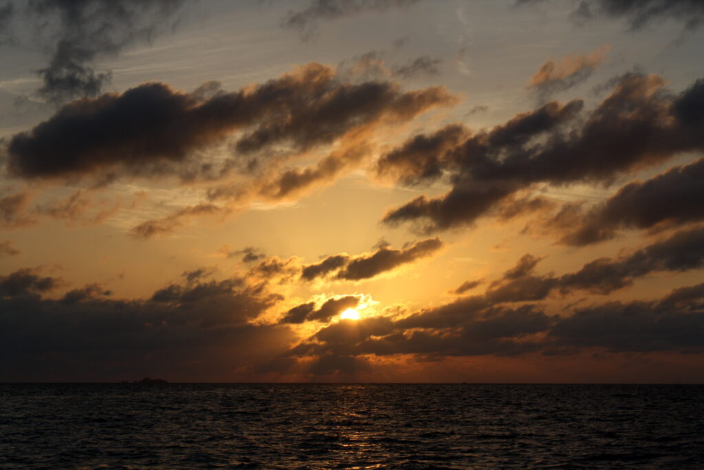 Sunset wallpaper with sun behind dark clouds casting orange gold hues over calm sea