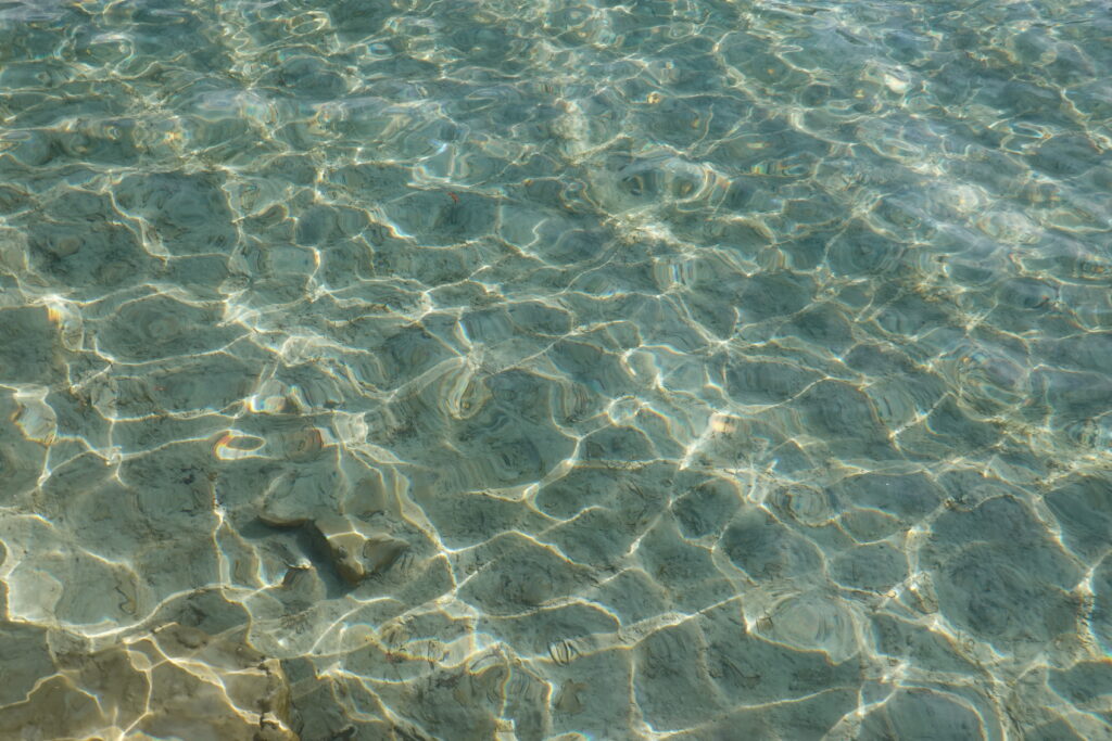 Transparent water with gentle ripples reflecting sunlight on clear shallow surface wallpaper background