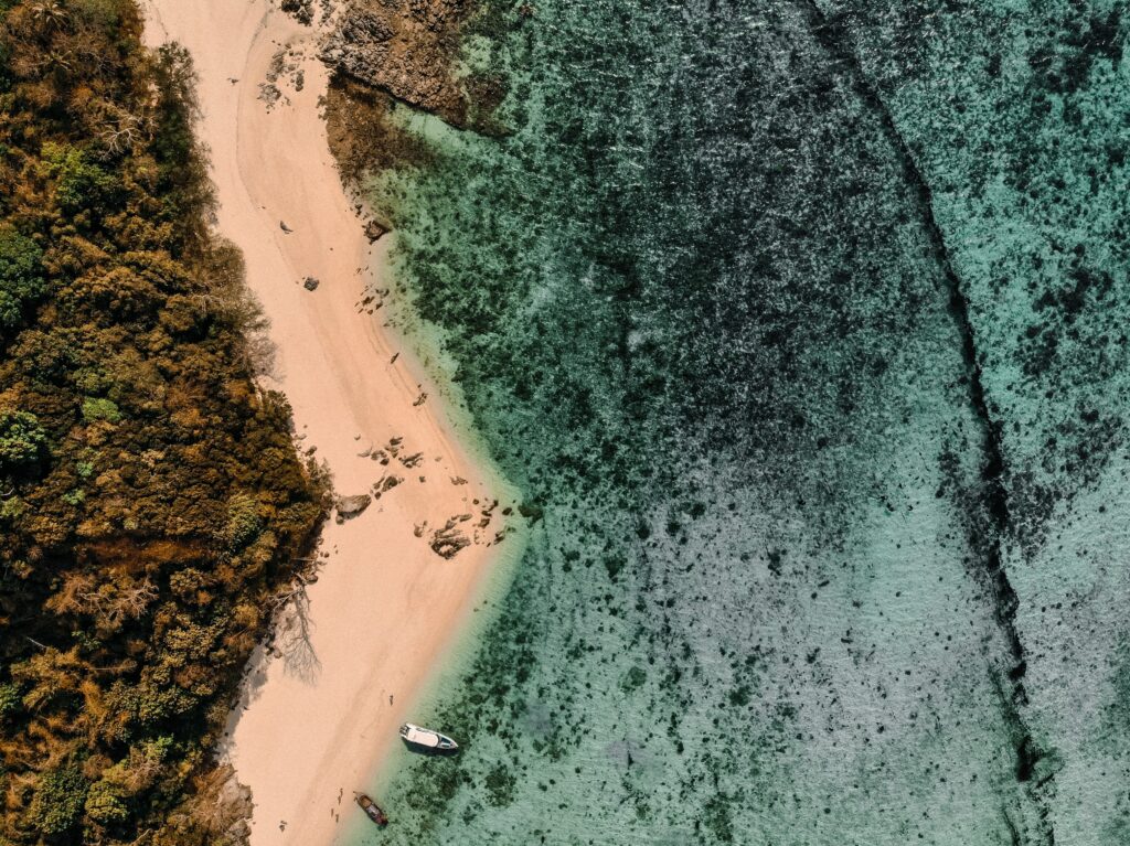 Aerial view of tropical beach with golden sand turquoise sea lush greenery and anchored boats Wallpaper