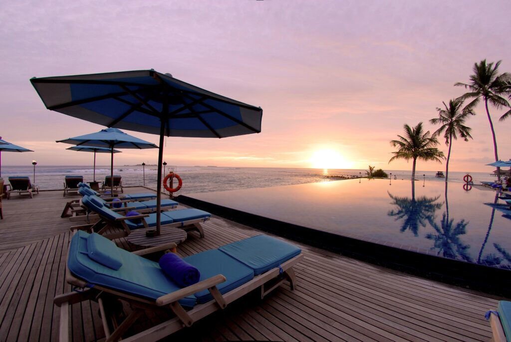 Serene tropical resort sunset with infinity pool wooden deck blue lounge chairs and palm trees Wallpaper