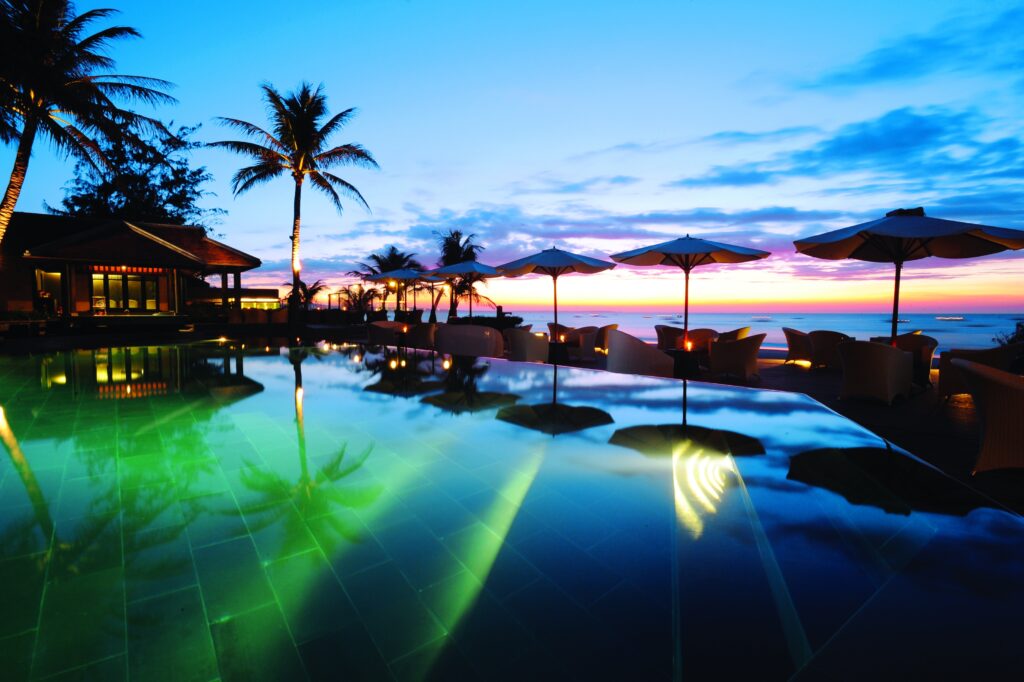 Tropical sunset seaside resort wallpaper with glowing pool reflections and palm tree silhouettes