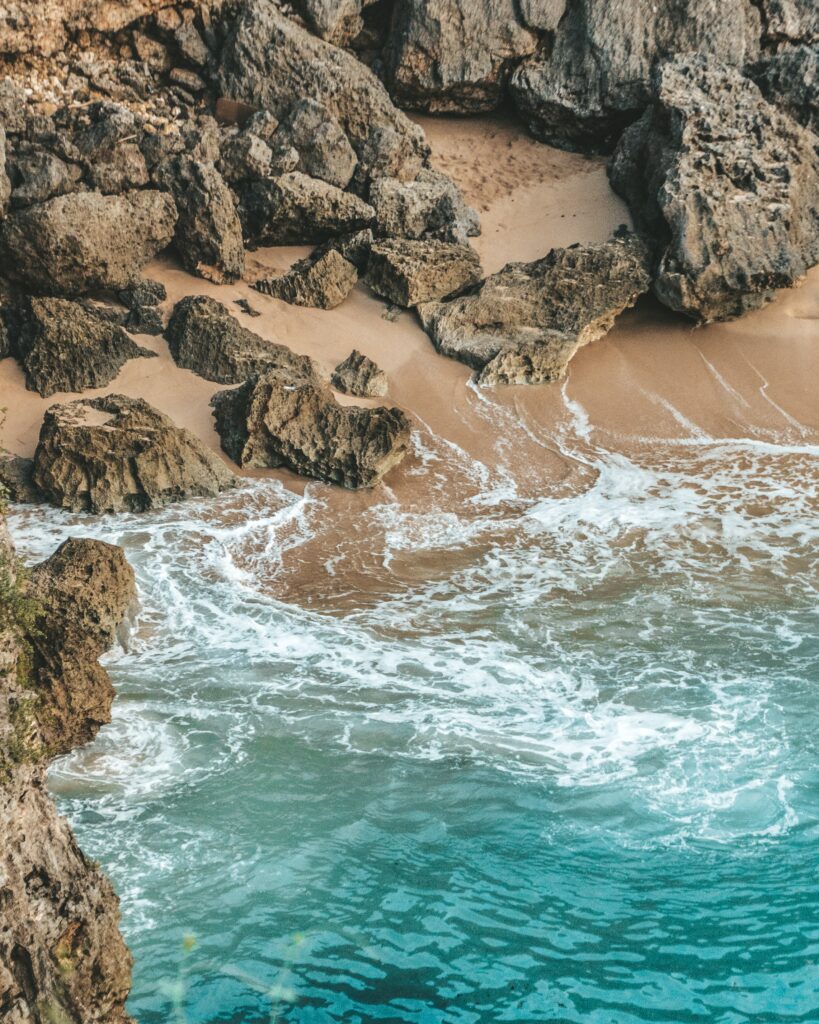Serene coastal wallpaper with turquoise sea washing sandy shores and rugged rocky textures