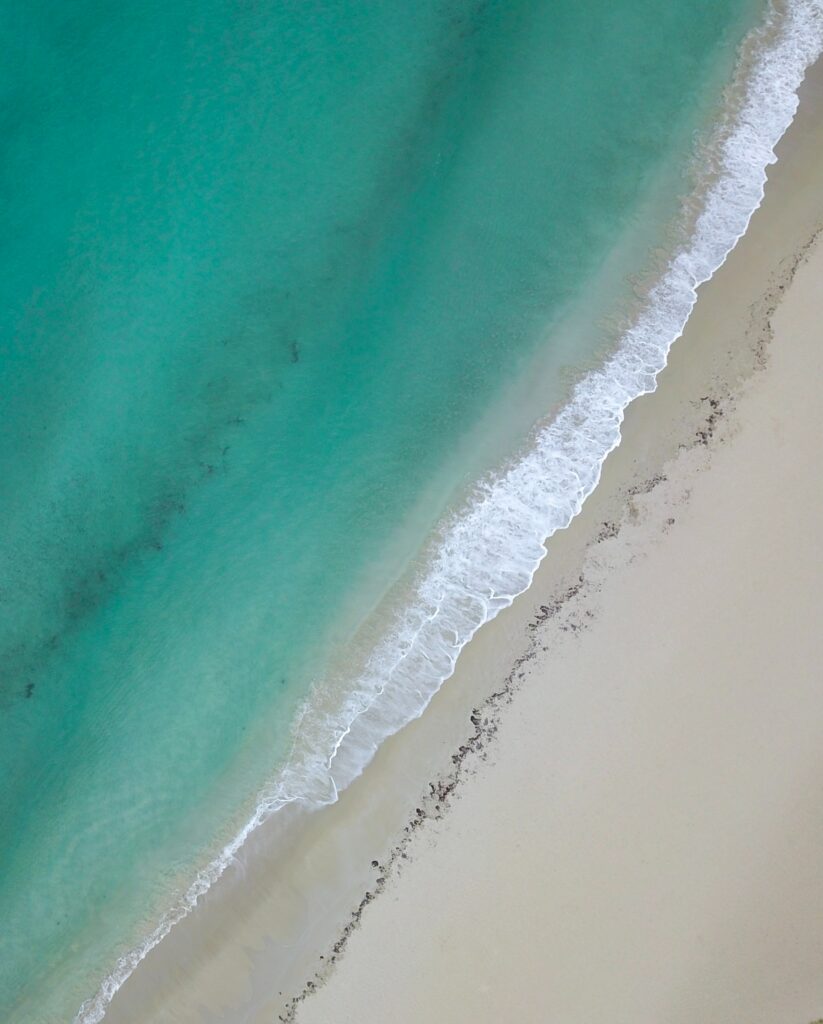 Aerial view of turquoise sea waves meeting soft pale sand on a serene minimalist coastline wallpaper