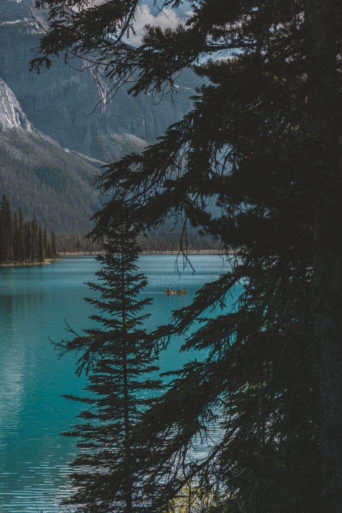 Photorealistic tranquil turquoise lake with mountains dense trees and a small boat floating Wallpaper