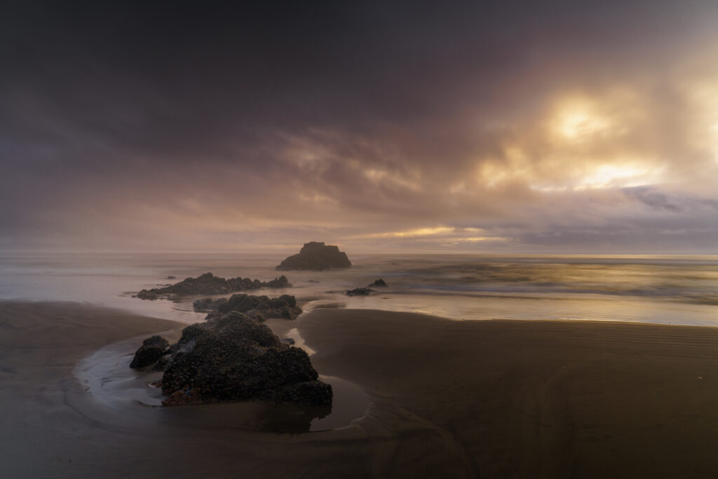 Twilight beach wallpaper with rocky shoreline soft waves and golden purple sky hues background