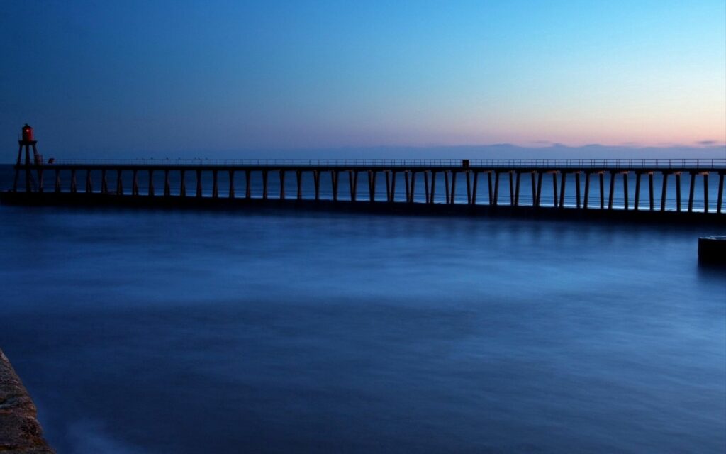 Serene twilight bridge over calm sea with beacon minimalist design soft blue hues wallpaper background
