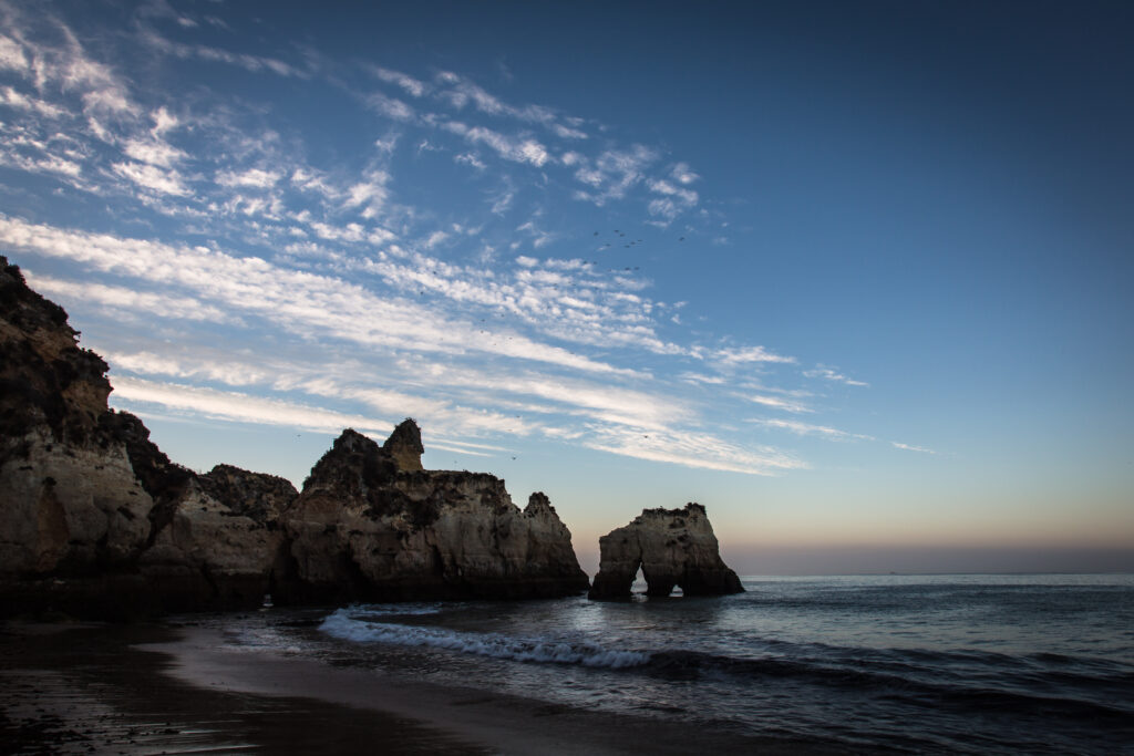 Serene twilight beach with rugged rocks gentle waves and tranquil sea under dusk sky wallpaper