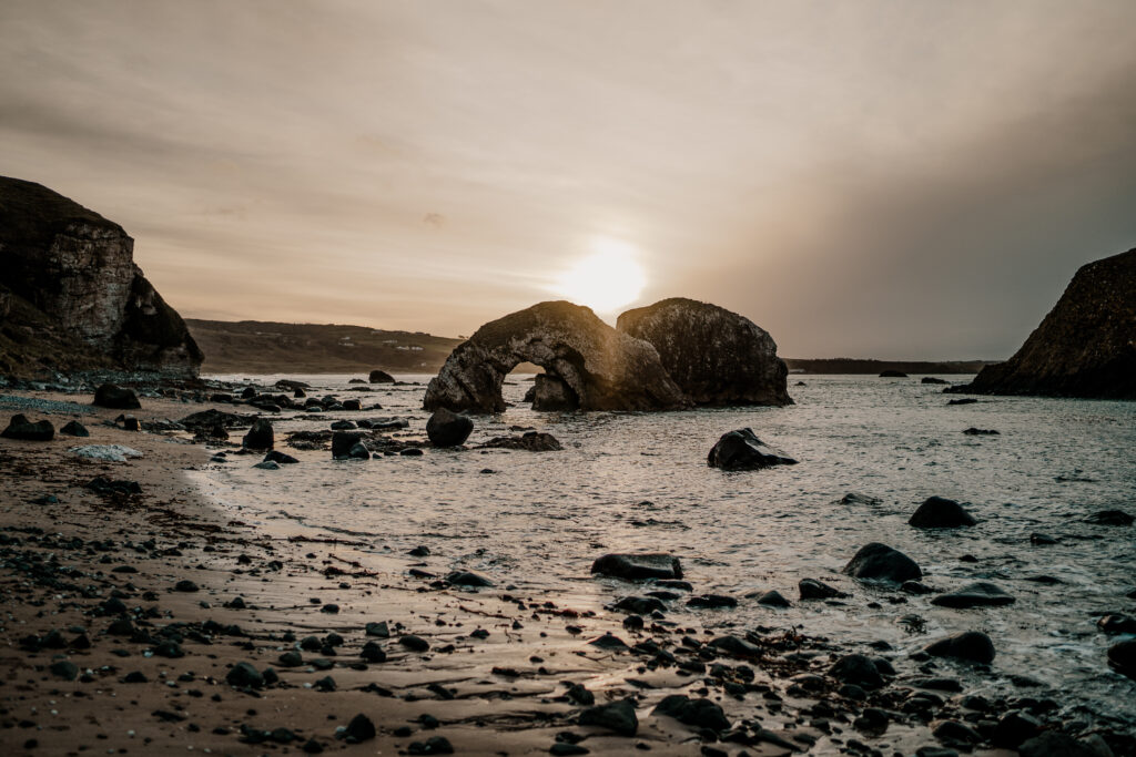 Twilight coastal wallpaper with stone arch rugged rocks calm sea golden sunset light serene view