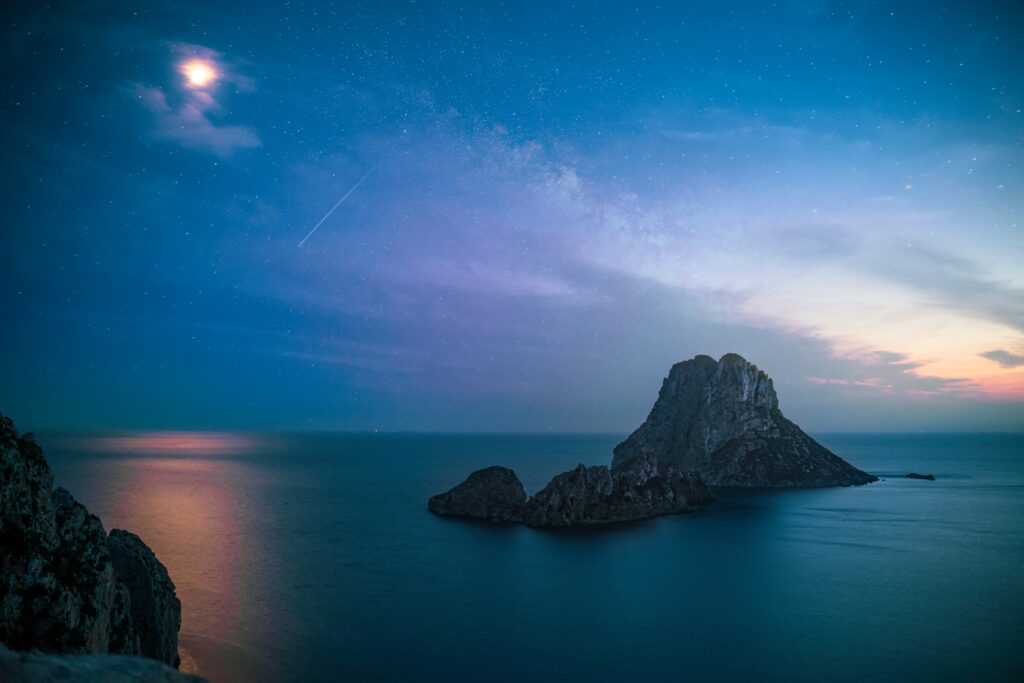 Serene evening coastal wallpaper with dramatic rock formation calm sea twilight sky stars moon