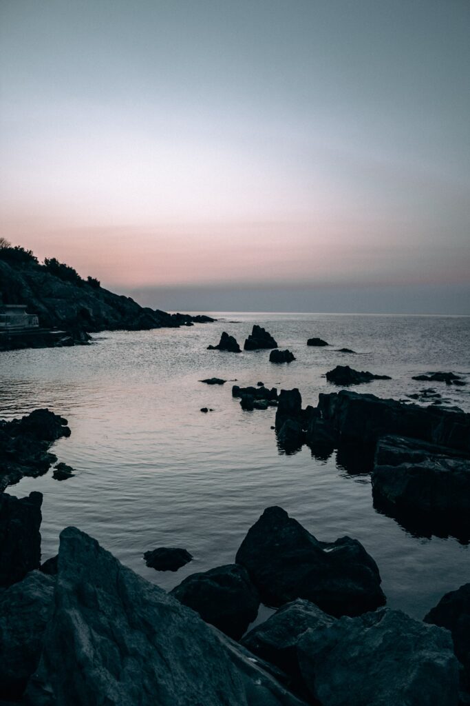 Serene twilight coastal scene with rugged rocks and calm waters in soft blue and pink hues Wallpaper