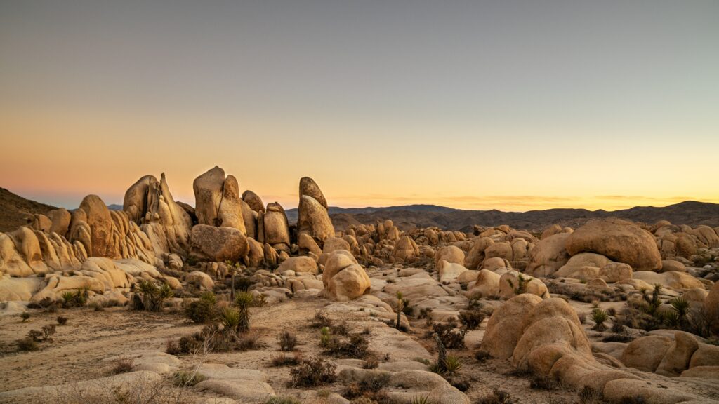 Serene twilight desert landscape with smooth weathered rocks under soft golden purple sky Wallpaper