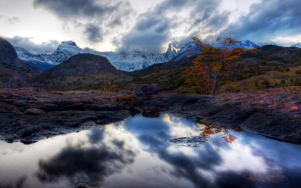 Twilight lake reflecting snow capped mountains vibrant orange tree and dramatic clouds landscape Wallpaper