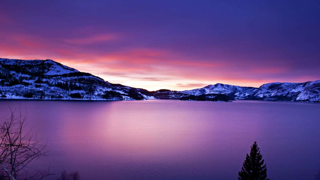 Serene lake at twilight reflecting purple pink sunset with snow-covered mountains winter landscape Wallpaper