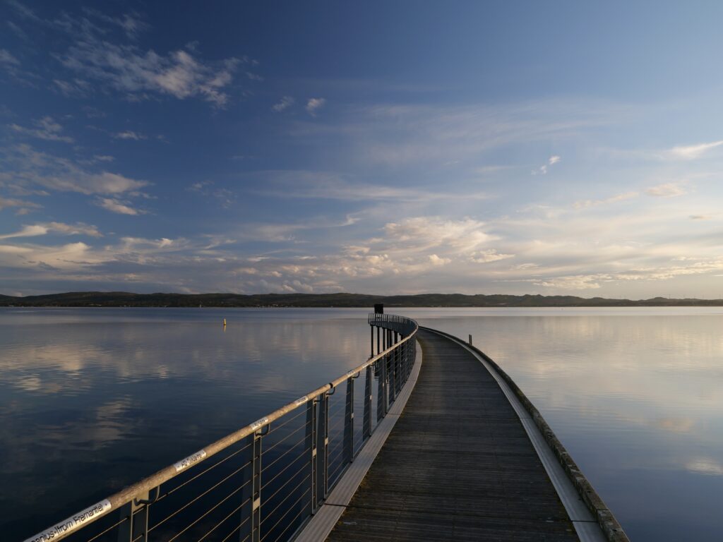 Serene twilight pier over calm water with warm sky reflections peaceful landscape wallpaper
