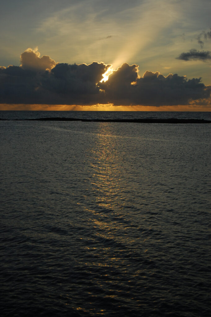 Serene twilight seascape with golden sun rays breaking through clouds reflecting on calm water Wallpaper