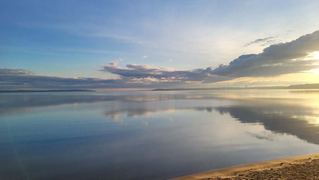 Serene twilight sea reflecting soft clouds and golden sunset glow peaceful wallpaper background