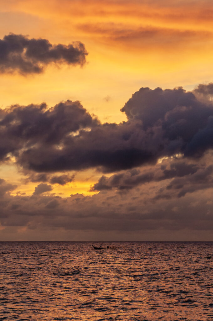 Small boat on calm sea under vibrant twilight sky with deep blues gold and orange hues serene view Wallpaper