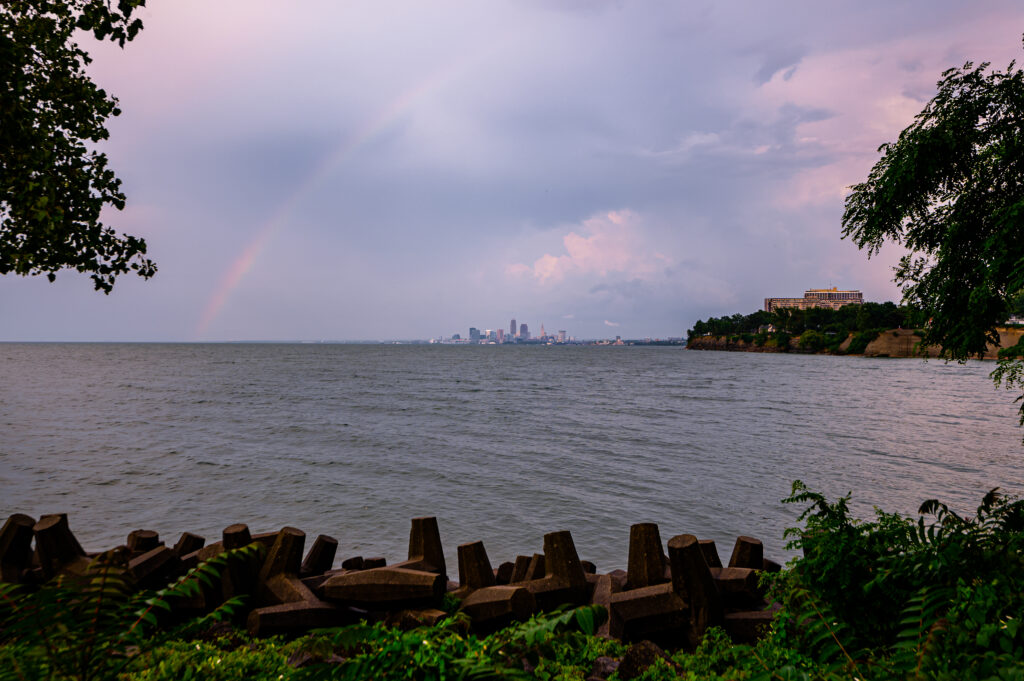 Serene twilight sea wallpaper with gentle waves rainbow greenery and distant city skyline background