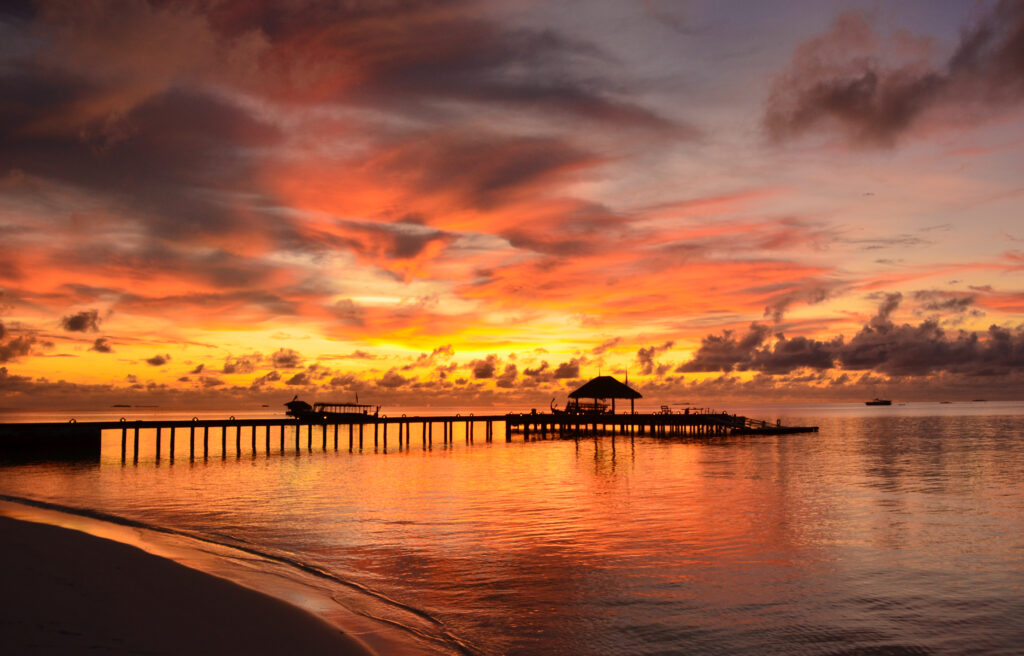 Wooden pier over calm sea at twilight with vibrant orange pink purple sunset reflections wallpaper